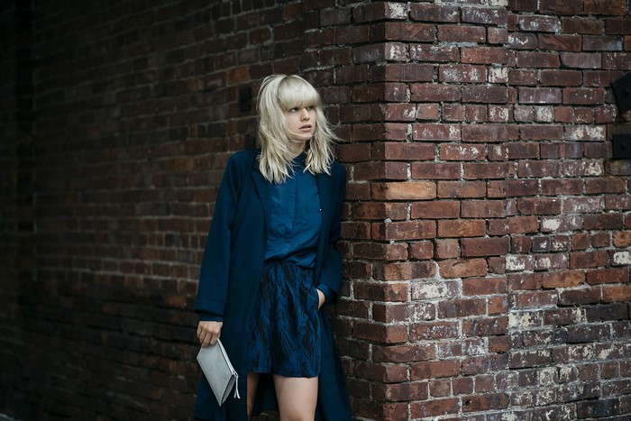 Woman in blue outfit leaning against brick wall