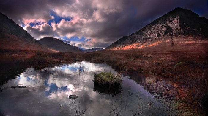 Mountain valley with a reflective pond and dramatic clouds