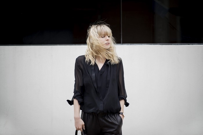Woman in black outfit standing against a wall