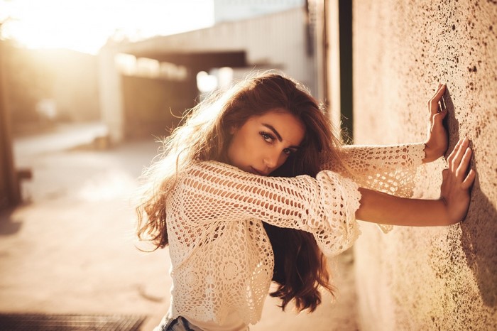 Woman with long brown hair leaning against a wall