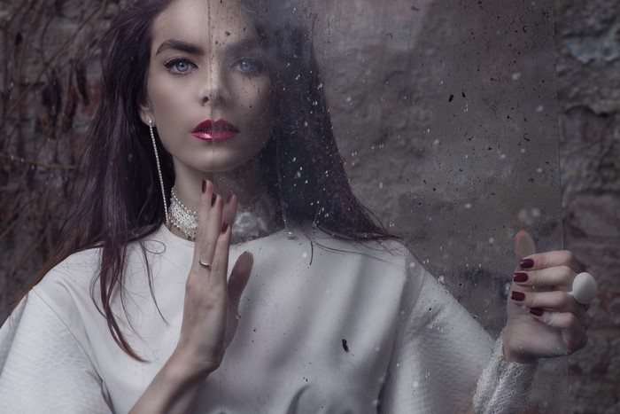 Woman with makeup and jewelry behind glass