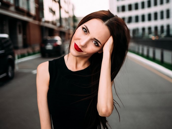 Woman with red lipstick and black dress posing outdoors
