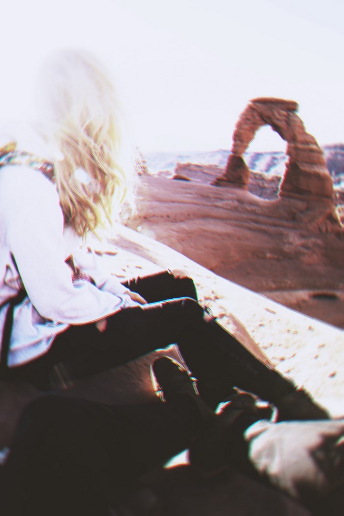 Woman sitting in a desert with Delicate Arch in the background