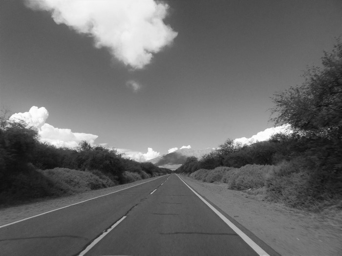Monochrome road through landscape with mountains and clouds