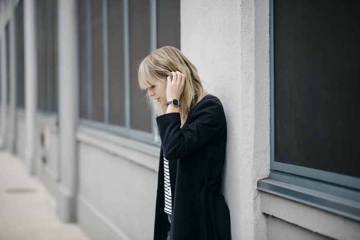Woman in black coat and striped shirt leaning against wall