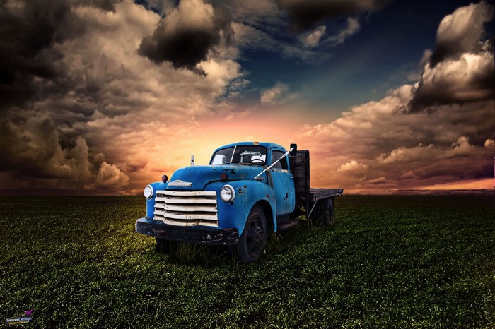 Blue vintage truck in a field at sunset