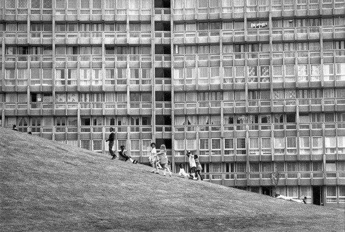Children playing on a grassy hill in front of Robin Hood Gardens