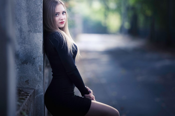 Woman in black dress leaning against a wall
