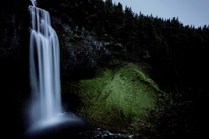 Waterfall cascading down a mossy cliff face in a dark forest