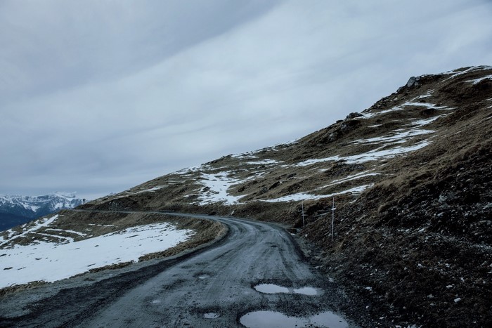 Winding mountain road with snow patches and cloudy sky
