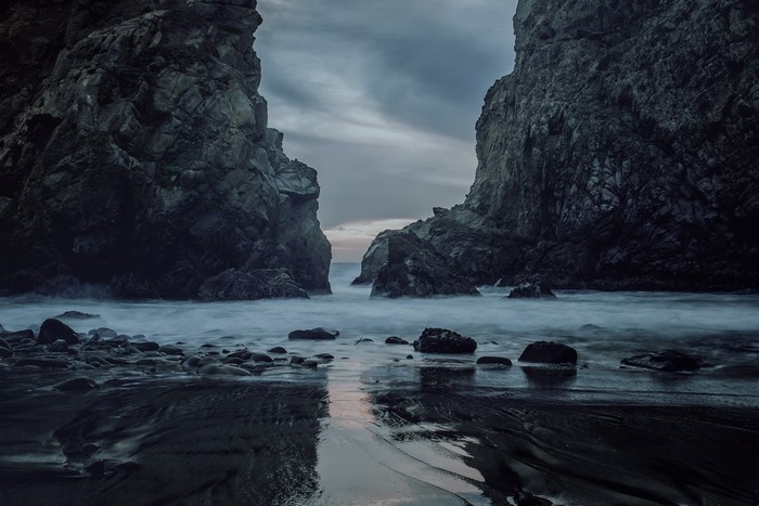Dark rocky coast with ocean waves at dusk