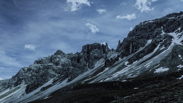 Rocky mountain range with snow patches under a cloudy sky