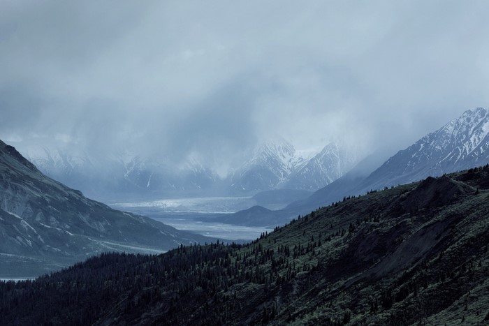 Misty mountain range with a glacier and forested slopes