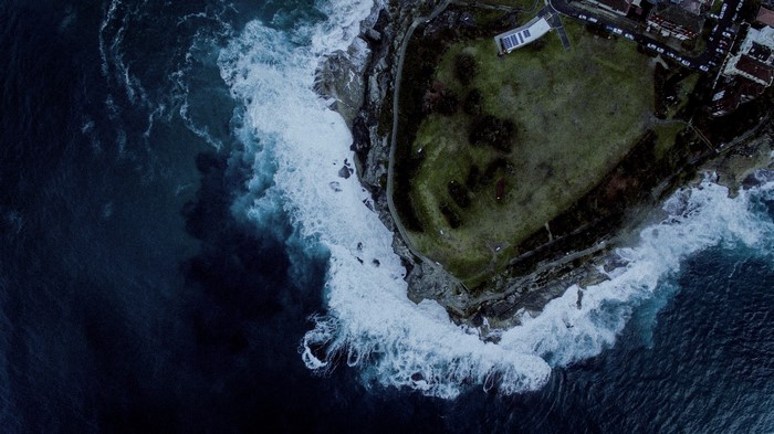 Aerial view of waves crashing on a rocky coastline with a grassy headland