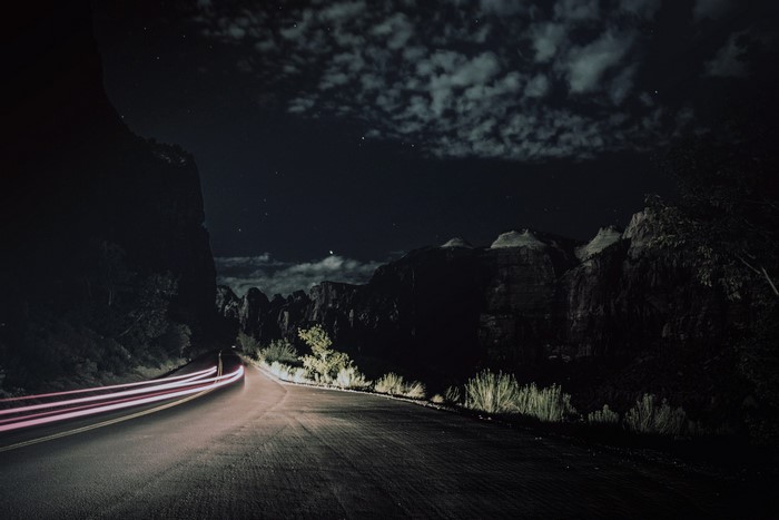 Night road with light trails and mountains under moonlight