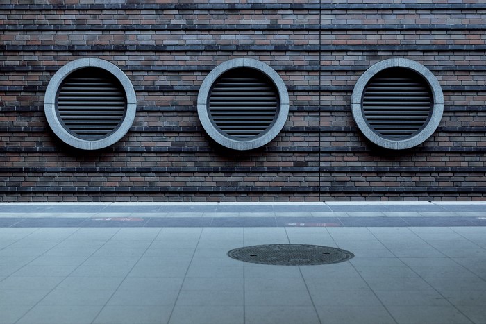 Three circular vents on a brick wall above a tiled floor