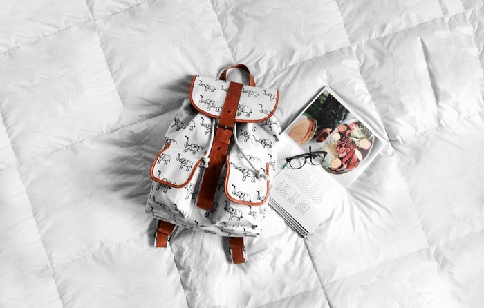 Backpack with elephant pattern on a white comforter with a magazine and glasses