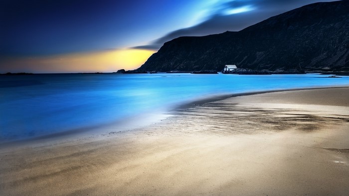 Beach with a small house and mountains at dusk