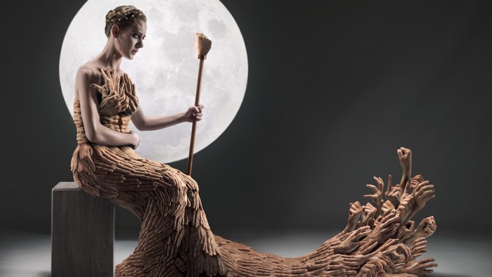 Woman in a dress made of hands holding a staff in front of the moon