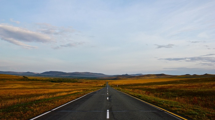 Empty road through a vast, grassy plain with mountains in the distance