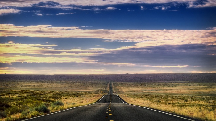 Long empty road through a vast grassy plain under a cloudy sky