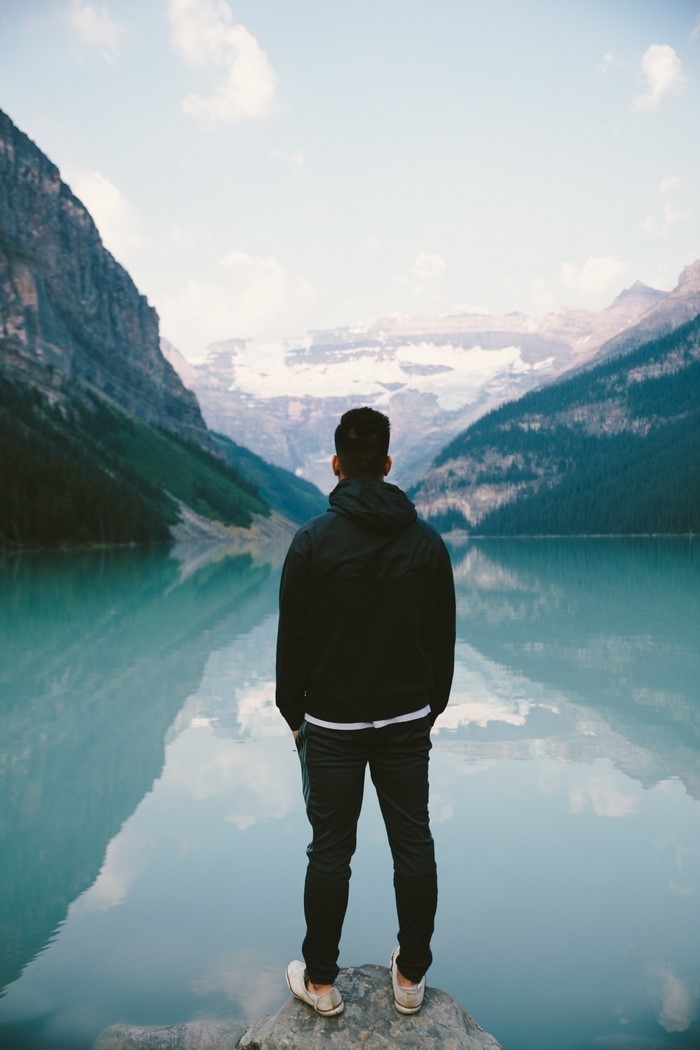 Man standing by a turquoise lake with mountains and glaciers