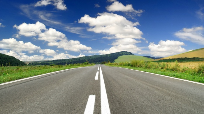 Empty road through rolling hills under a blue sky