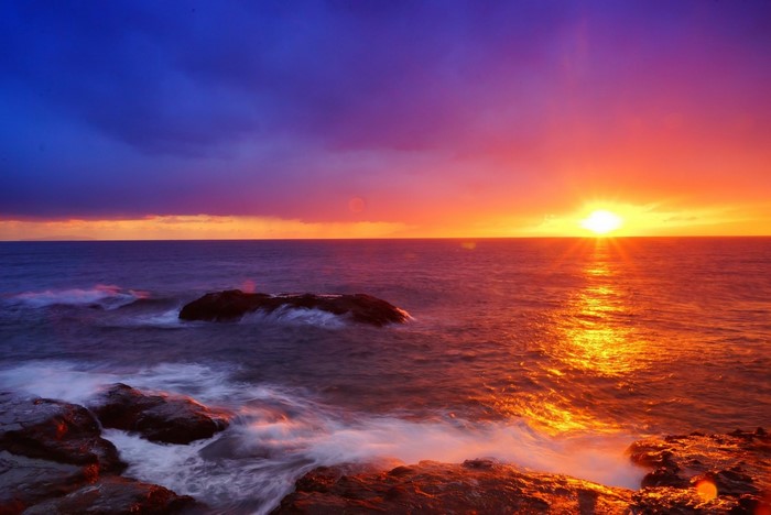 Sunset over the ocean with waves crashing on rocks