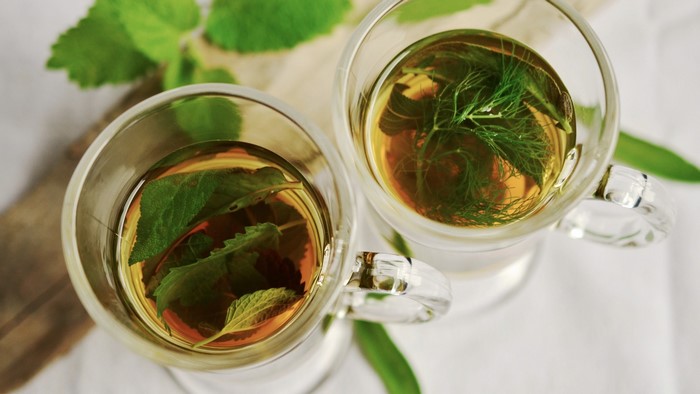 Two cups of herbal tea with fresh herbs