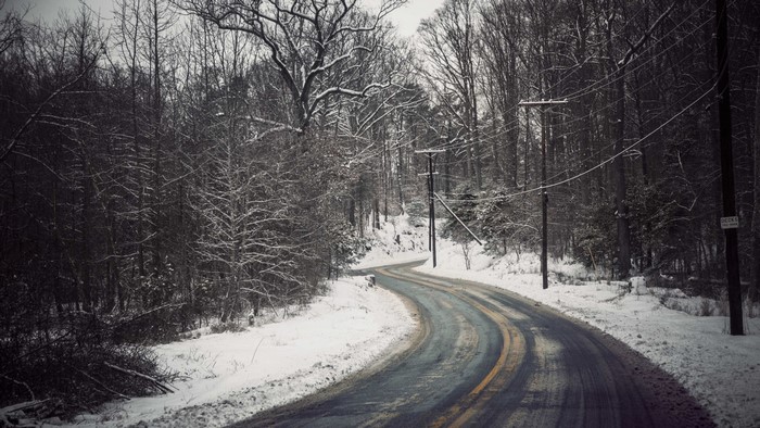 Winding snowy road through a winter forest with power lines