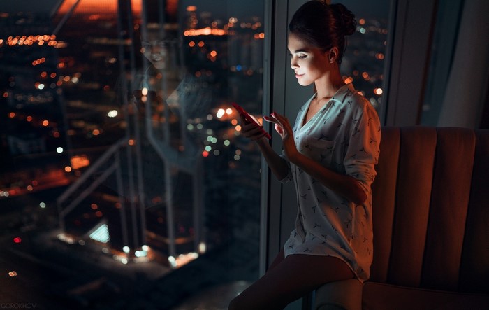 Woman looking at cellphone by window at night