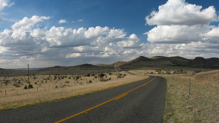 Road through a dry, hilly landscape under a cloudy sky