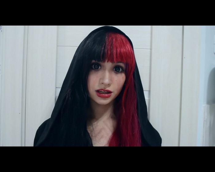 Woman with split black and red hair wearing a black hood