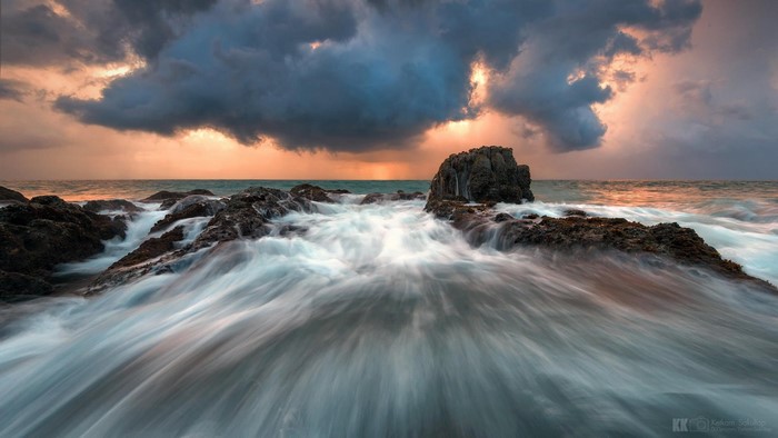 Waves crashing on rocks at sunset with storm clouds