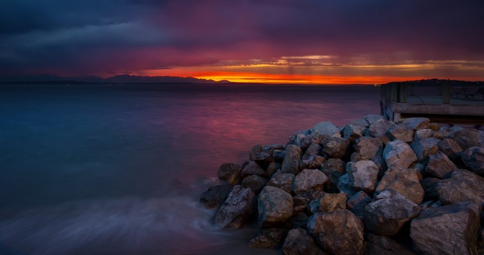 Sunset over the ocean with rocks and a pier