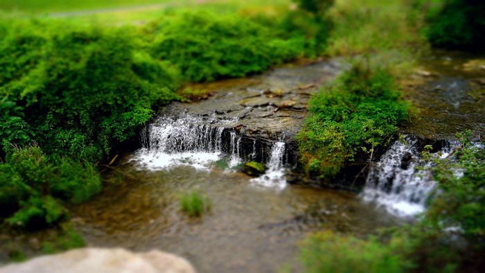 Miniature waterfall in a lush green forest with tilt-shift effect