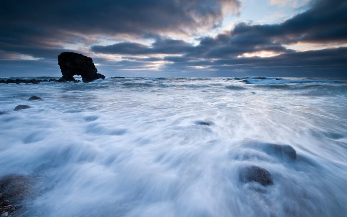 Sea arch rock formation on a rocky shore with waves