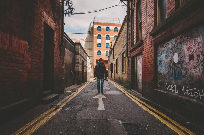 Man walking down a graffiti-covered alleyway in a city