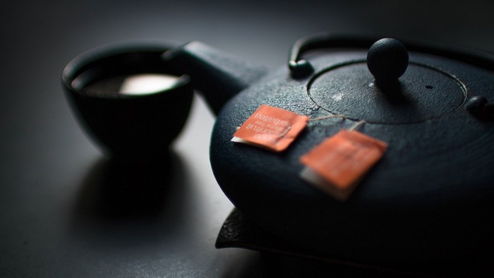 Close up of a black teapot with tea bags and a cup