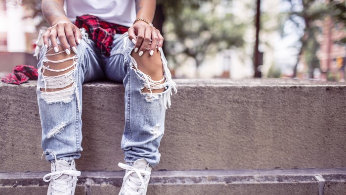 Person wearing ripped jeans and white sneakers