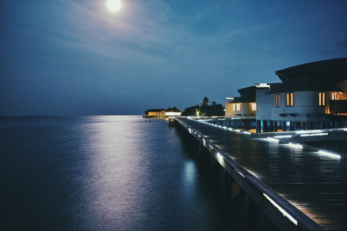Overwater bungalows at night with moon reflection on the sea
