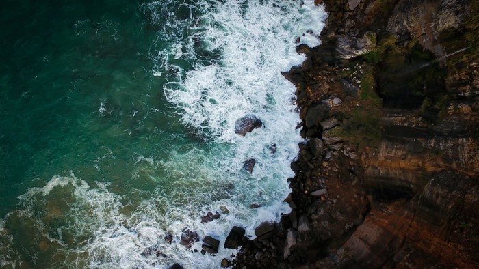 Aerial view of ocean waves crashing on rocky shore