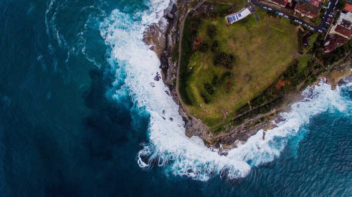 Aerial view of waves crashing on a rocky coast with a grassy headland