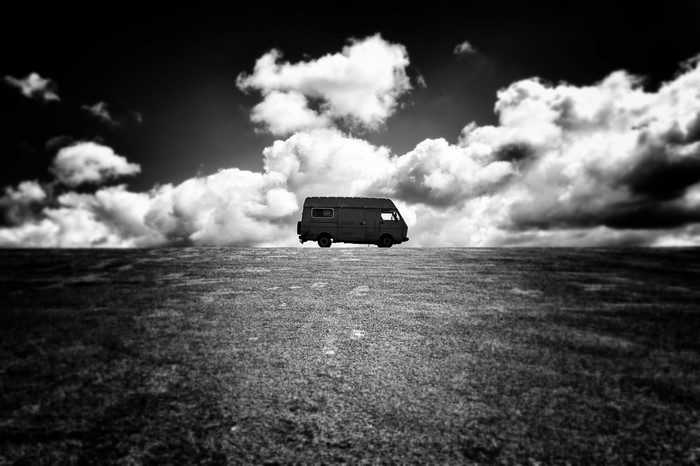Monochrome image of a van on a grassy field under a cloudy sky