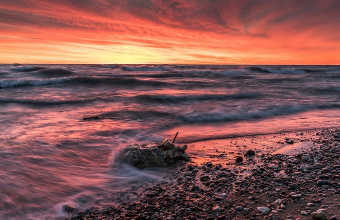 Sunset over the ocean with waves crashing on a rocky shore