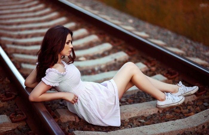 Woman in white dress sitting on railway tracks