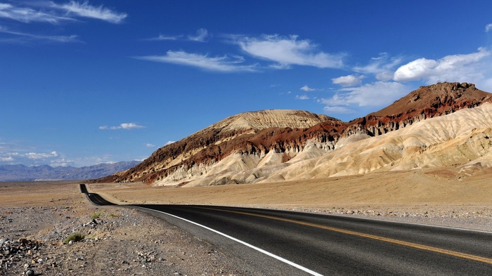 Desert road leading to colorful mountains under a blue sky