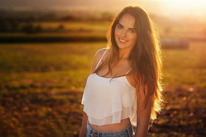 Woman in white crop top and jeans smiling in field