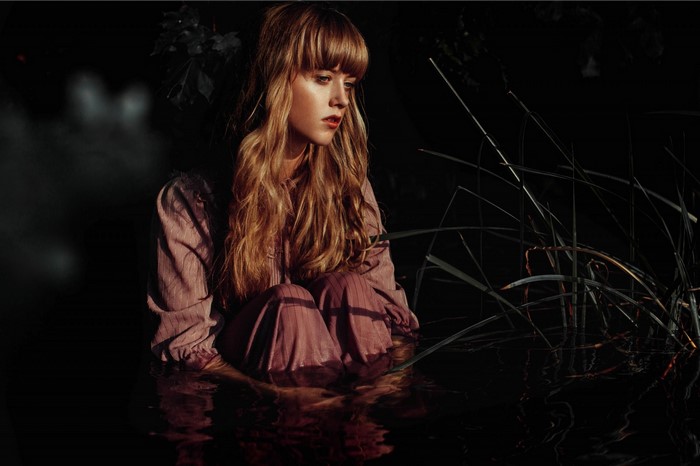 Woman sitting in dark water with reeds