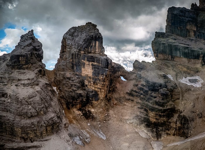 Rocky mountain peaks with a natural arch under a cloudy sky